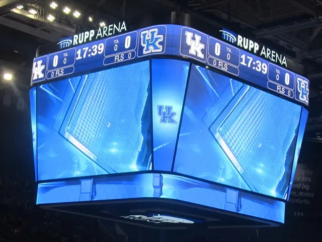 The image shows a large screen in the middle of a basketball court, surrounded by a group of people...