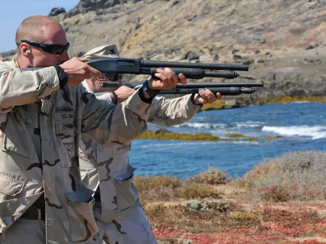The image shows two men in camouflage uniforms shooting shotguns on the beach, with a hill in the...