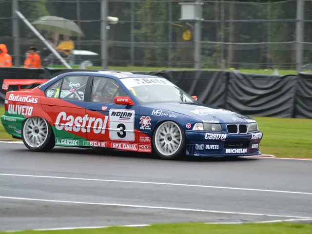 The image shows a car driving on a race track with text and numbers on it, surrounded by grass on...