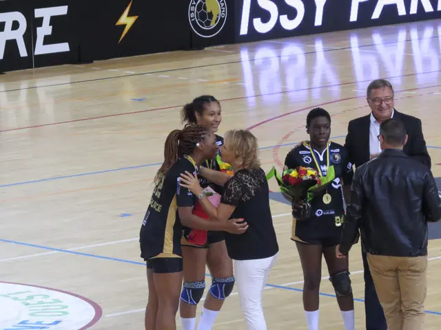 The image shows a group of women standing on top of a basketball court, with two of them holding...