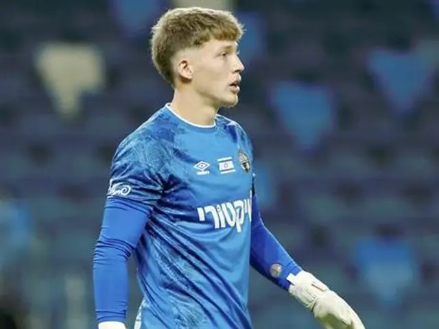 The image shows a young man in a blue goalkeeper's uniform standing on a soccer field, with a...