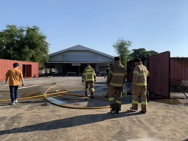 The image shows a group of firefighters standing in front of a building with a hose, surrounded by...