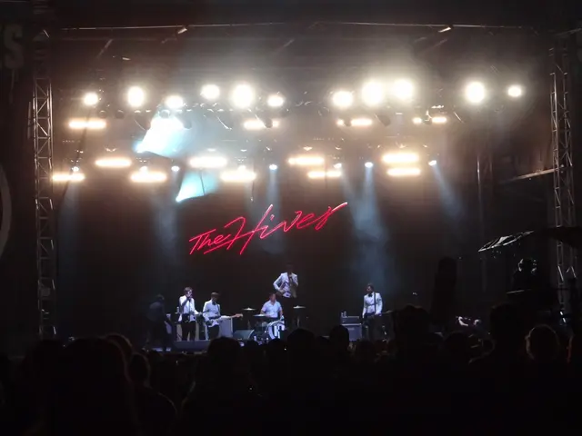 The image shows a group of people on stage at a concert, with some of them holding musical...