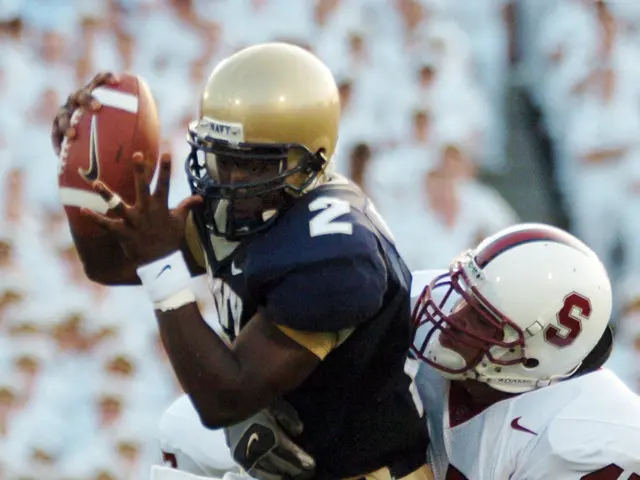 The image shows a football player catching a ball in the air while being tackled by another player....