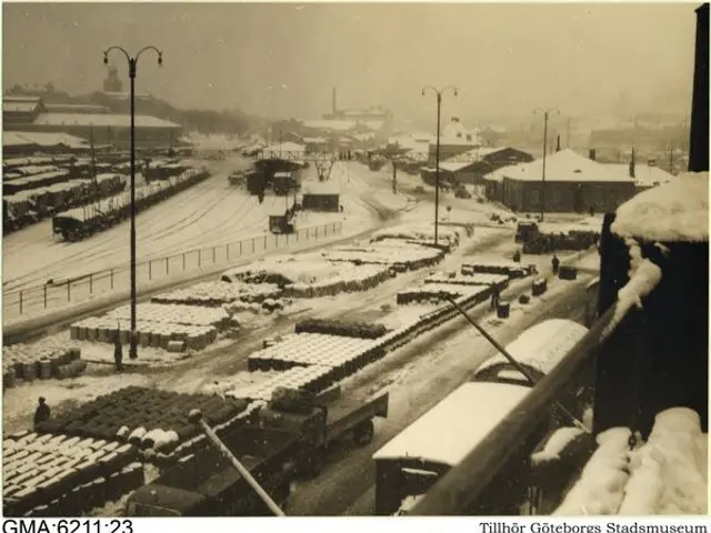 The image shows a black and white photo of a city street covered in snow. We can see vehicles on...