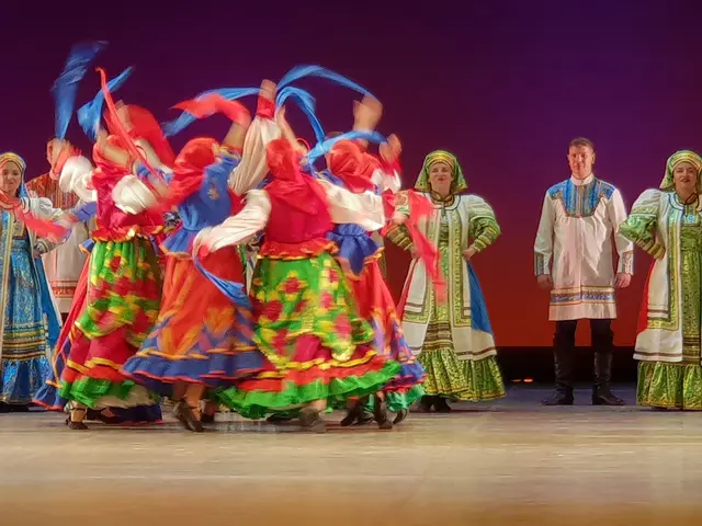 The image shows a group of people in colorful dresses dancing on a stage, with a wall in the...