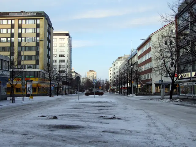 The image shows a city street covered in snow with tall buildings in the background. There are...
