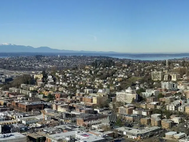 The image shows a panoramic view of Seattle from the top of a hill. We can see many buildings,...