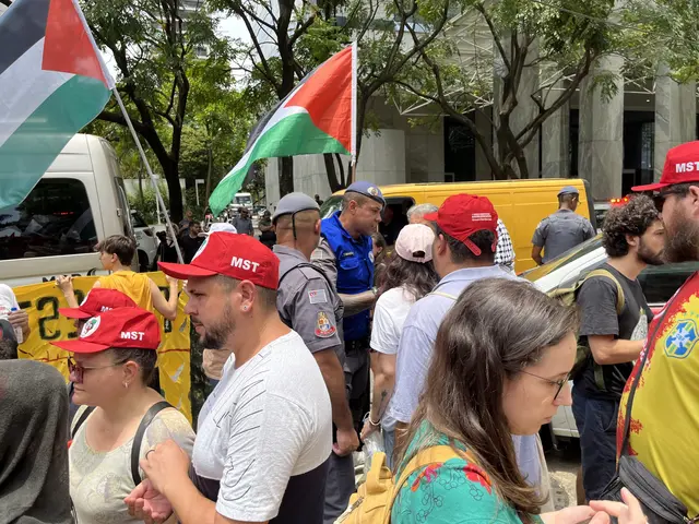 The image shows a group of people standing in front of a building, some wearing caps and some...