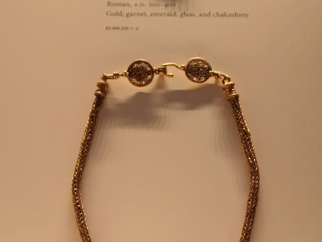 The image shows a gold necklace with a pendant on display in a museum. The pendant is in the shape...
