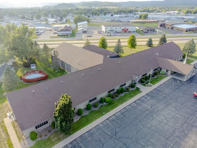 The image shows an aerial view of a large building with a parking lot in front of it, surrounded by...