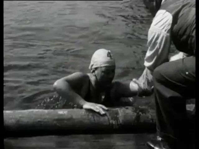 The image shows a black and white scene of a man in the water with a bandage on his head,...