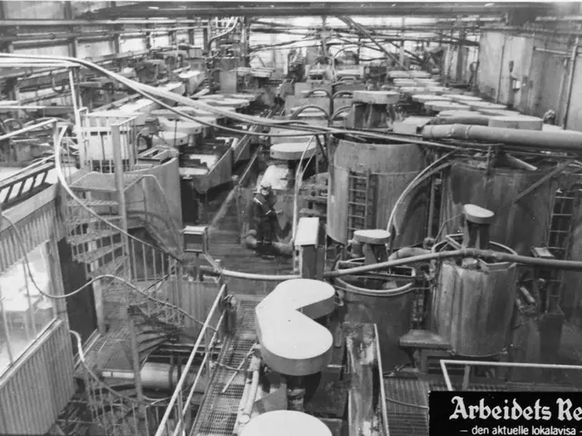 The image shows a black and white photo of a factory with a person standing on the floor surrounded...
