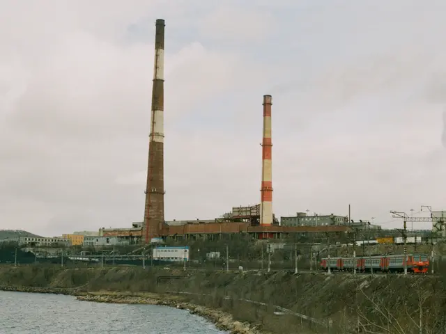 The image shows a coal-fired power plant situated next to a body of water, with a train on the...