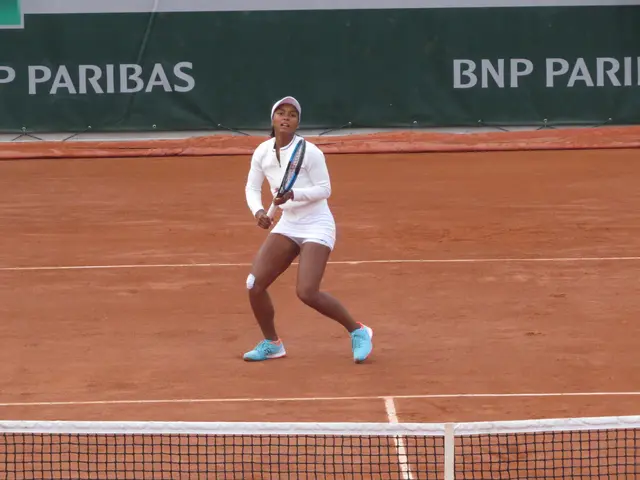 The image shows a woman in a white dress playing tennis on a clay court. She is holding a tennis...