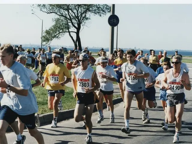 The image shows a group of people running in a marathon on a road surrounded by grass, trees, light...