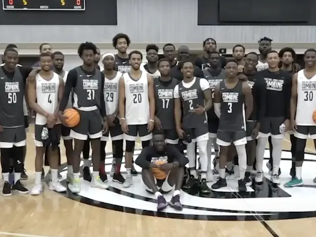 The image shows a group of men standing on top of a basketball court, with some of them holding...