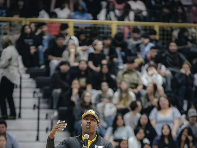The image shows a man standing on top of a basketball court, wearing a cap and holding a...