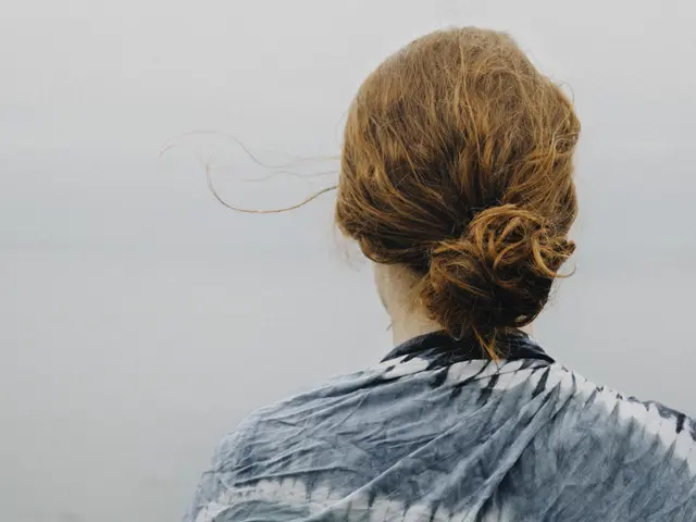 The image shows a woman with red hair wearing a blue and white tie dye shirt, standing in front of...