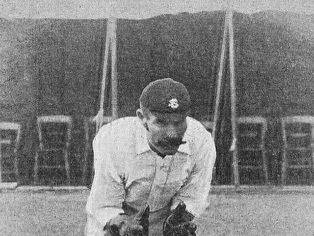 The image shows a black and white photo of a man playing a game of cricket. He is wearing a cap,...