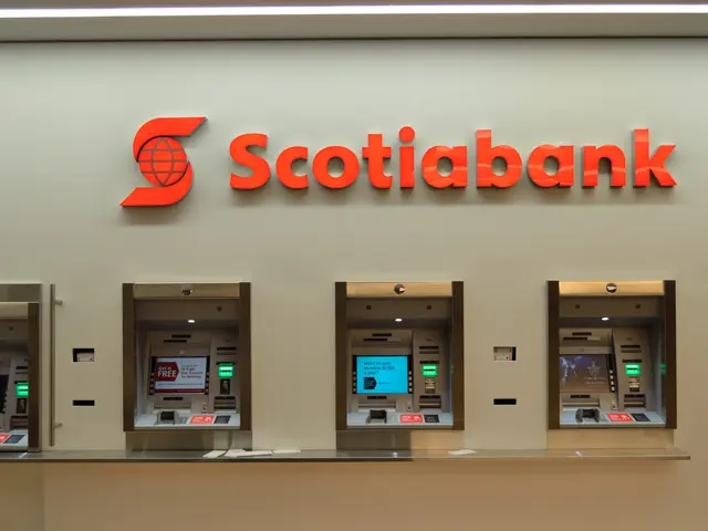 The image shows a scotiabank ATM machine in a bank, with a wall in the background featuring text...