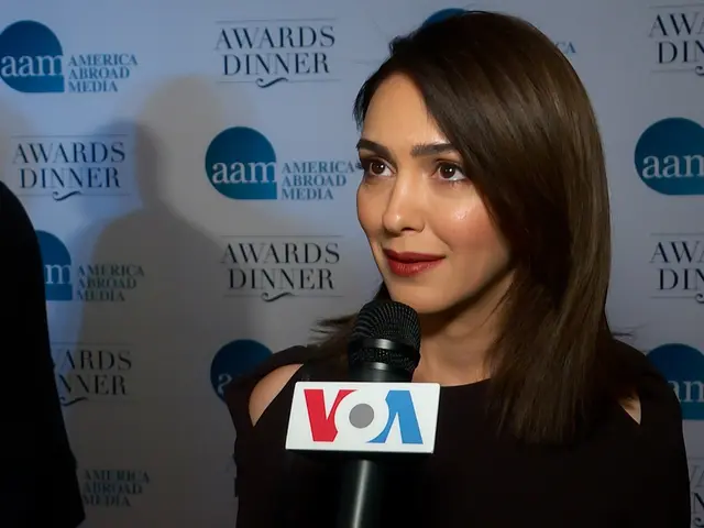 The image shows a woman in a black dress holding a microphone, with a man standing to her left and...