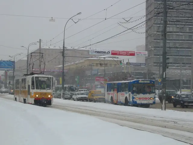 The image shows a city street filled with lots of traffic on a snowy day. We can see vehicles on...