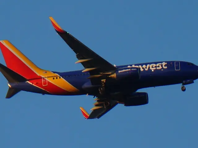 The image shows a Southwest Airlines plane flying in the sky with its landing gear down, its wings...