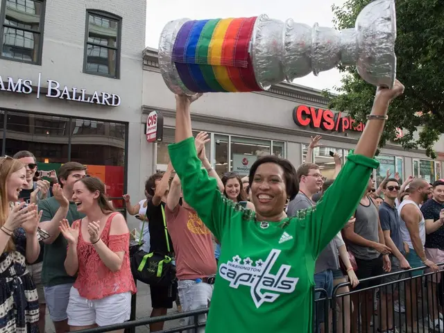 The image shows a woman holding up a Stanley Cup in front of a crowd of people, some of whom are...