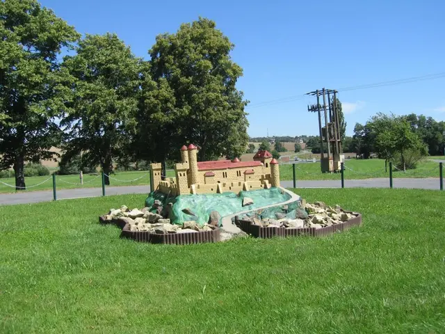 The image shows a miniature golf course in the middle of a grassy field, surrounded by a fence with...
