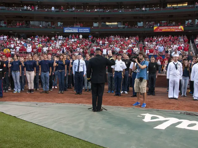 The image shows a man standing on top of a baseball field next to a crowd of people. He is wearing...