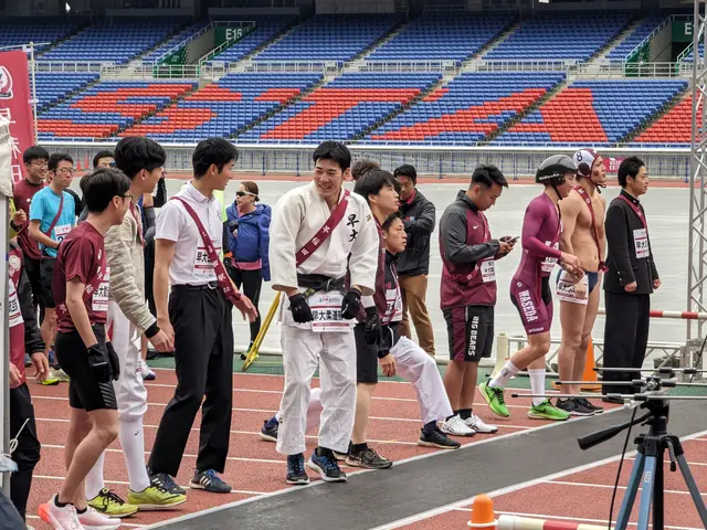 The image shows a group of people standing on top of a track, with a camera on a tripod stand to...