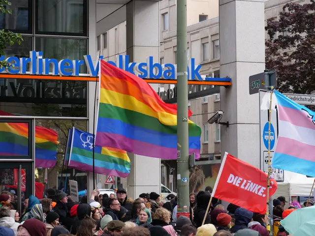 The image shows a large group of people standing in front of a building, holding flags and banners...