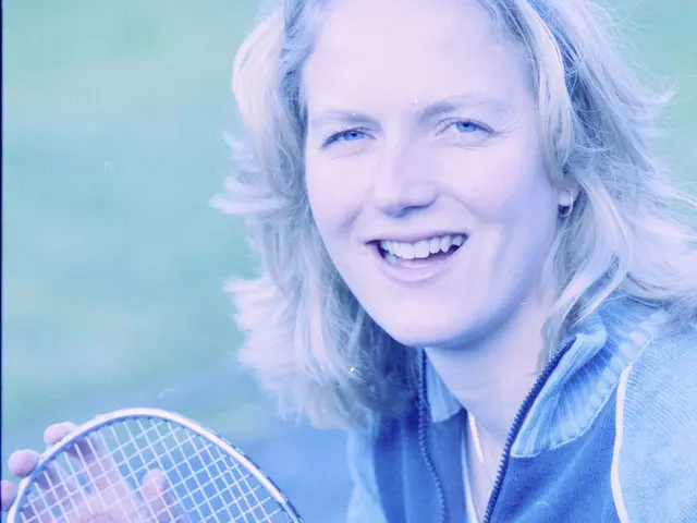 The image shows a woman with a bright smile on her face, holding a badminton racket in her hand....
