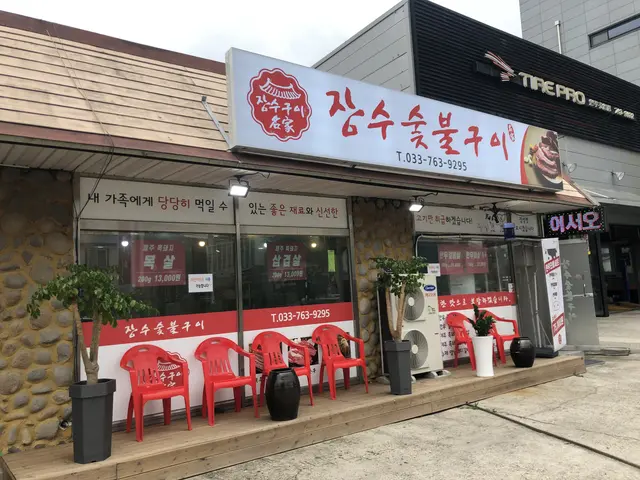 The image shows a restaurant with red chairs outside of it, surrounded by plants in pots, a...