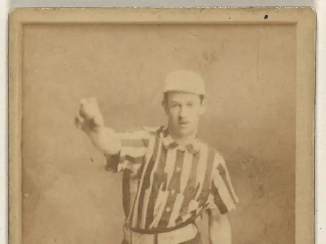 The image shows an old photo of a man in a referee's uniform, wearing a cap and standing in the...