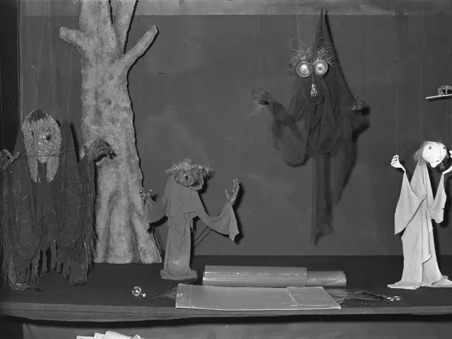 The image shows a black and white photo of a group of puppets on a table in front of a wall. On the...