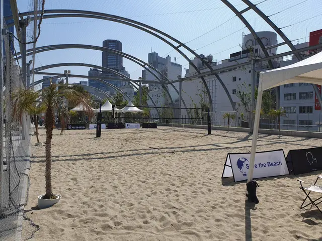 The image shows a beach volleyball court with a net and chairs set up in the sand, surrounded by...