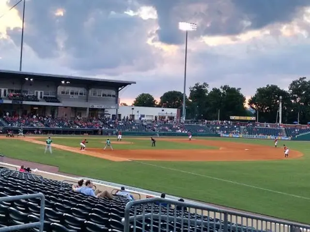 The image shows a baseball game being played in a stadium, with people sitting in the stands and a...