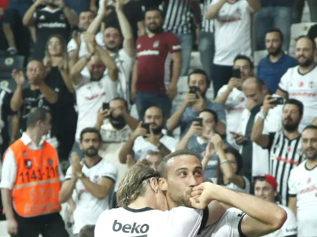 The image shows two soccer players celebrating a goal in front of a cheering crowd. They are...