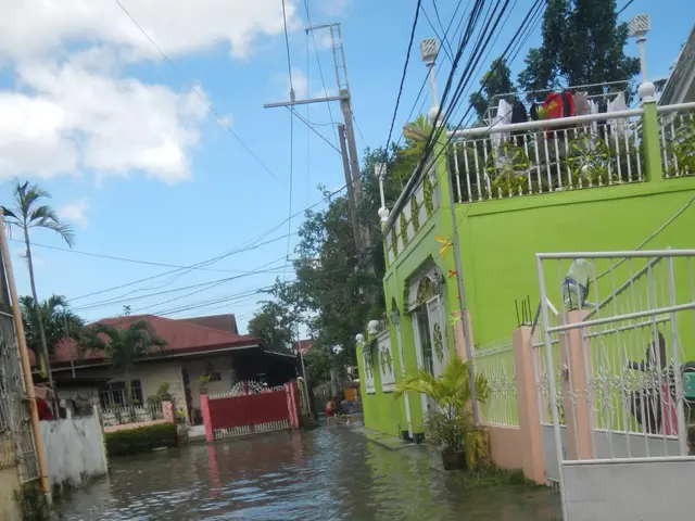 The image shows a flooded street in the Philippines with buildings on either side, railings,...