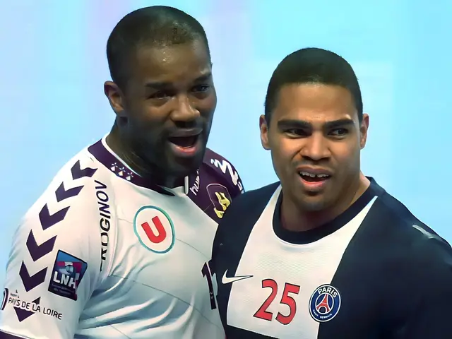 The image shows two men standing next to each other on a soccer field, both wearing white and blue...