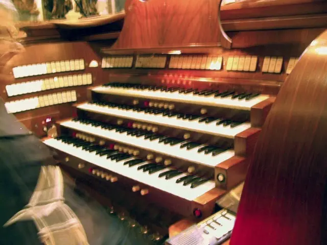 The image shows a man playing an electric organ in a church. He is standing in front of the pipe...