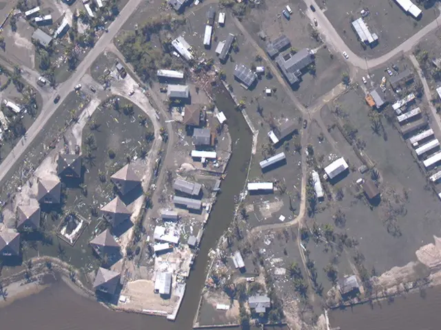 The image shows an aerial view of a city with lots of buildings, trees, roads, vehicles, and water,...