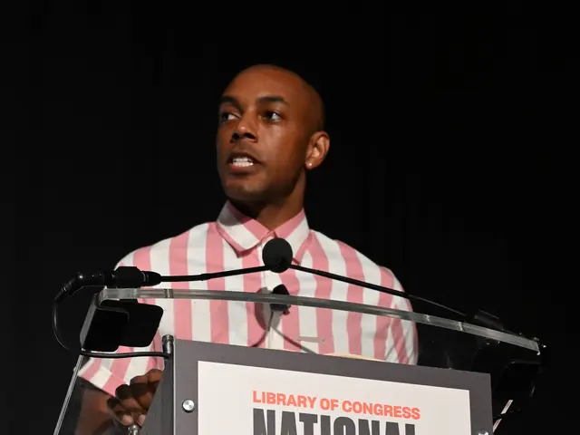 The image shows a man standing at a podium in front of a sign that reads "National Book Festival...