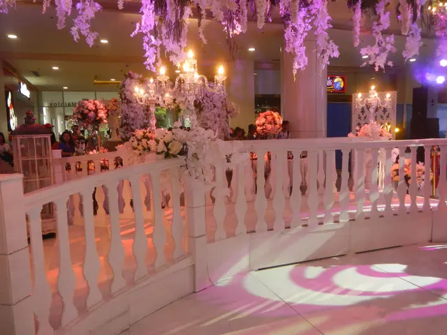 The image shows a wedding reception with a white railing adorned with flowers and chandeliers...