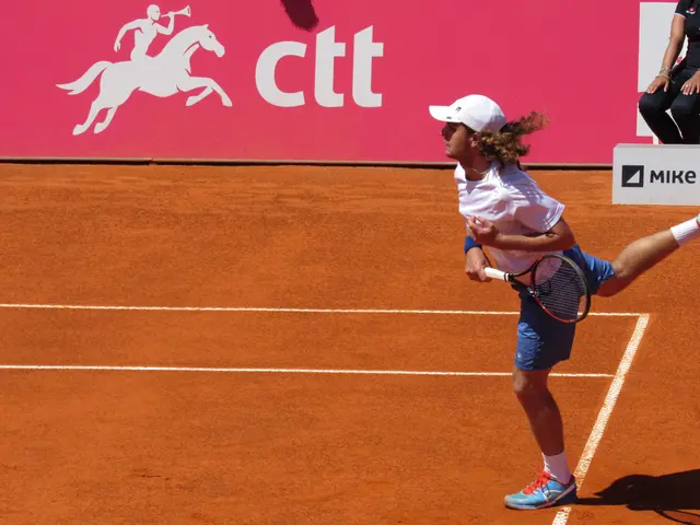 The image shows a man in a white shirt and blue shorts playing tennis on a clay court. He is...