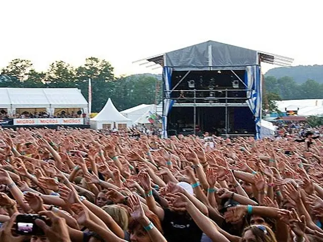 The image shows a large crowd of people at a music festival with their hands in the air, some of...
