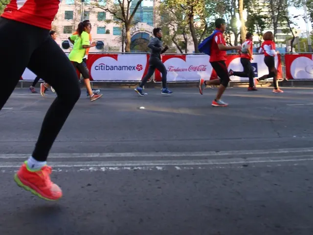 The image shows a group of people running in a marathon on a road surrounded by trees, buildings...