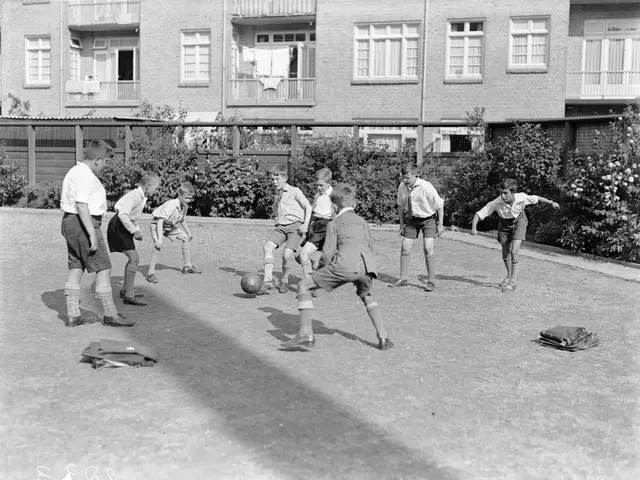 The image shows a group of young boys playing soccer on a grassy field, with a ball in the center....